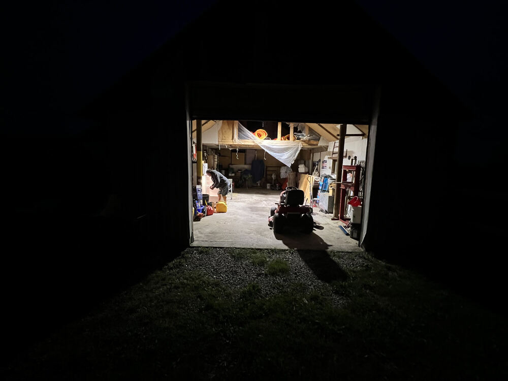A black night yard with one bright rectangle at its centre: an open garage, lit from within, its contents visible and its light spilling a short way onto the grass.